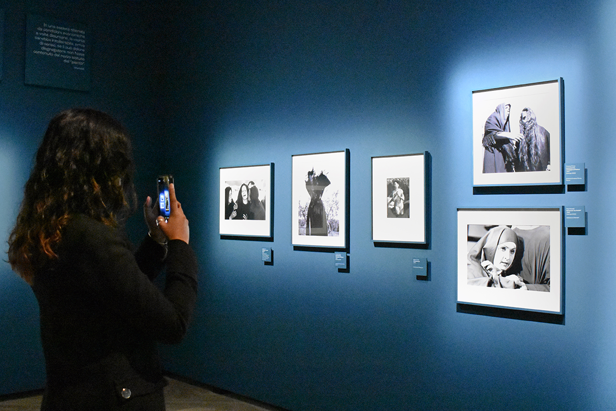 Student taking a photograph of framed images hung on a blue wall.