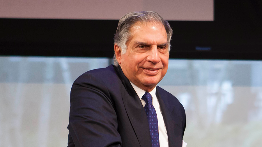 A smiling man with graying short hair man in a black suit and tie.