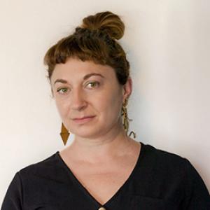 Woman looking ahead wearing a black V-neck shirt and gold earrings.