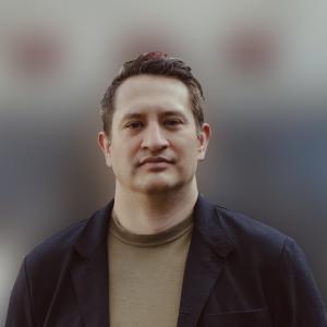 A person wearing a dark black jacket in front of a blurred background.