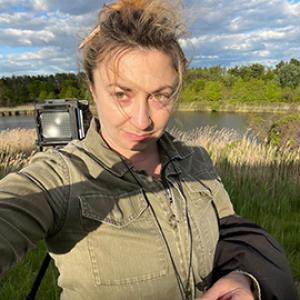 Woman with green shirt in an outdoor scene with camera equipment. 