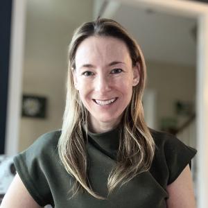 Woman smiling at the camera with blond hair and an olive green dress.