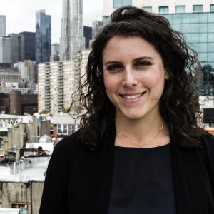 a person with dark long hair wearing a black shirt with a city in the background