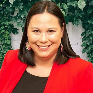 Woman with straight black hair wears a black top under a bright red jacket with coordinating earrings