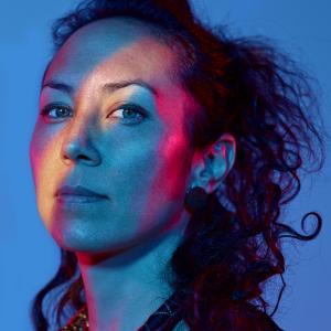 A woman in three-quarter profile with long dark hair pulled up in a loose ponytail.