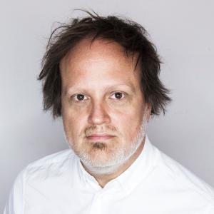 A man with dark hair and a grey goatee looking at the camera