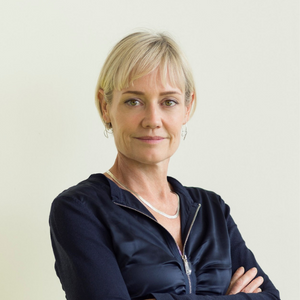 A woman with short blonde hair standing in front of a plain white wall