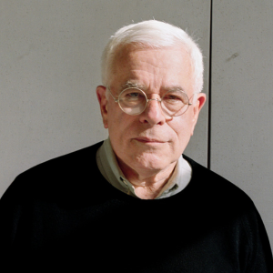 A man with white hair wearing glasses looking seriously at the camera