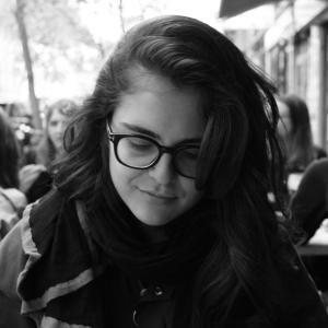 A black and white photo of a woman wearing glasses and looking down. She is smiling