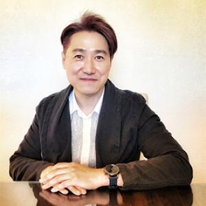 Man wearing a white button down shirt and black jacket, smiling.