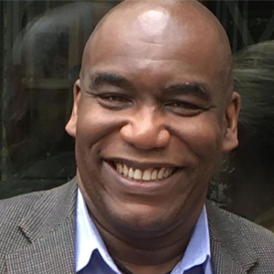 A man smiling with a grey suit and blue dress shirt.
