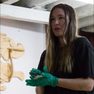 Image of woman with long hair, green gloves, dark shirt holding something in her hand.