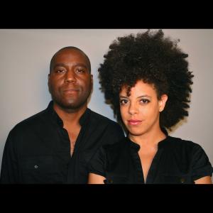 One person in a dark black long sleeve shirt next to another person with a lot of curly black hair wearing a short sleeve black shirt.