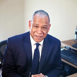 man sitting at a desk wearing a suit and a navy tie