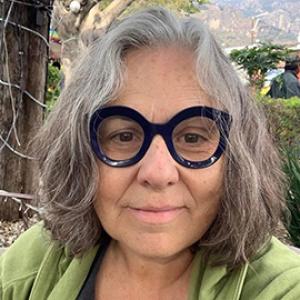 Woman with grey hair, big black glasses and a green shirt.