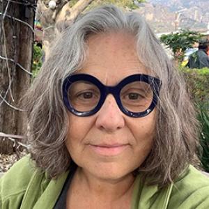 Woman with grey hair, big black glasses and a green shirt.