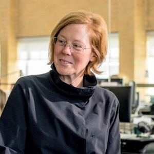 A woman with red hair and glasses wearing a dark blue jacket 