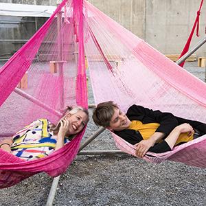 two people sitting in pink hammocks.