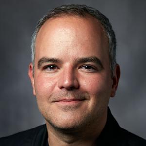 A light skinned man with short gray hair and a black shirt.