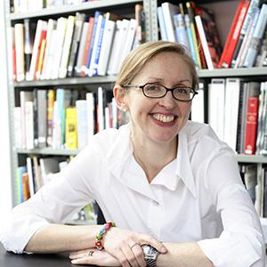 Blond woman wearing white button down blouse and black glasses seated in front of a bookcase