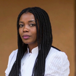 A portrait of a woman with long dark hair staring into the camera in front of a soft brown background