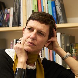 woman with short brown hair resting her head in her hand in front of a bookcase