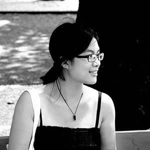 A black and white picture of a woman with glasses smiling and not looking at the camera