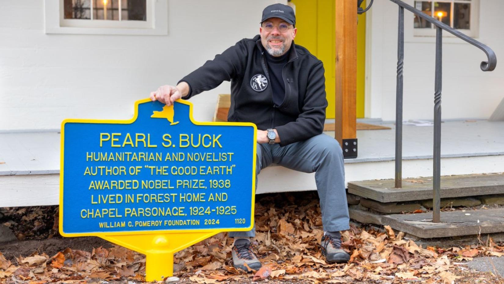 a man sitting next to a large blue and yellow historical sign