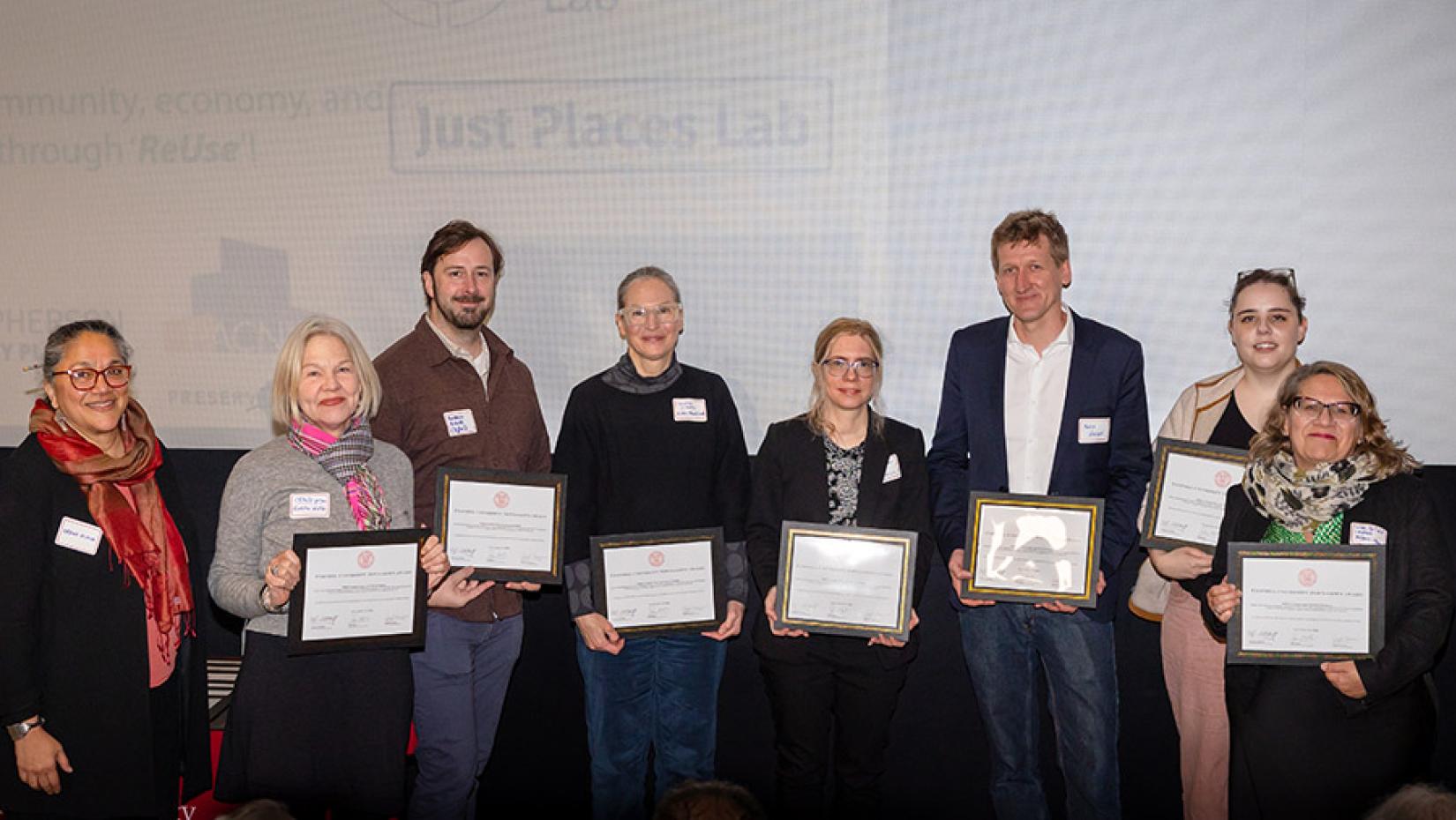 A large group of people holding up awards in front of a movei thetre screen.