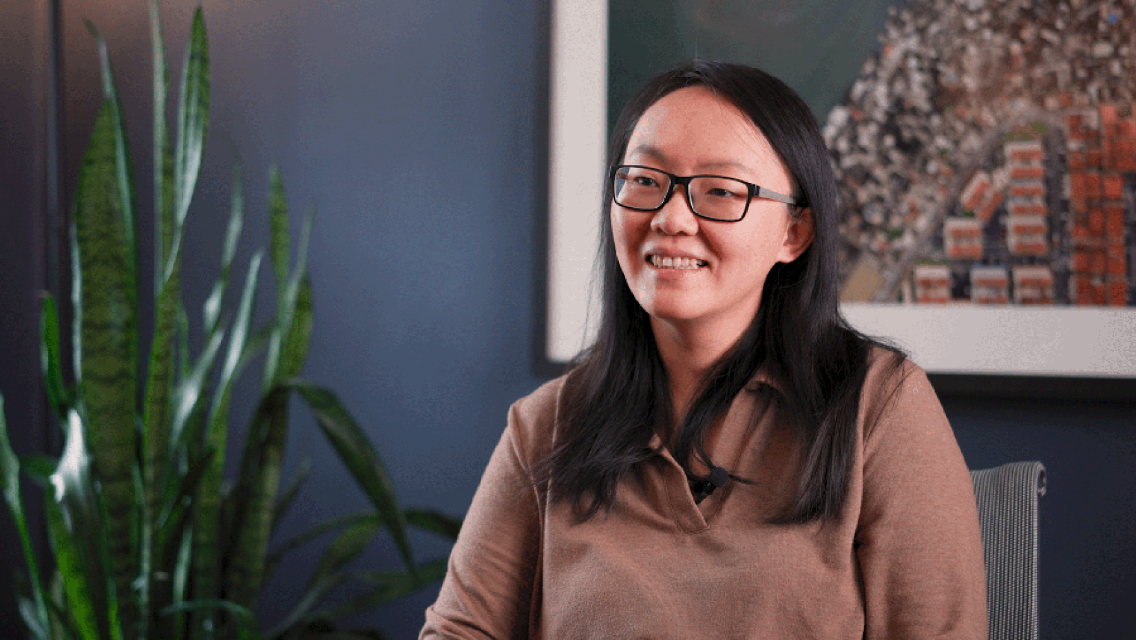 Asian woman with long dark hair wearing glasses and a tan sweater seated for an interview