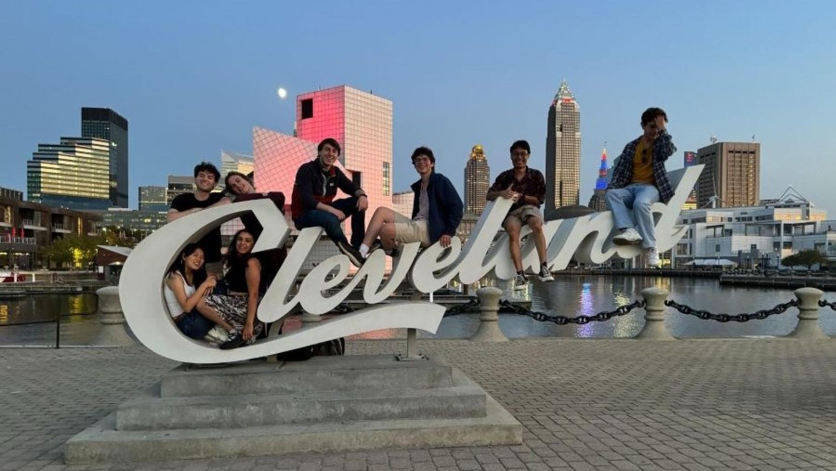 A group of students sitting on a large sign that says Cleveland with the city skyline in the background