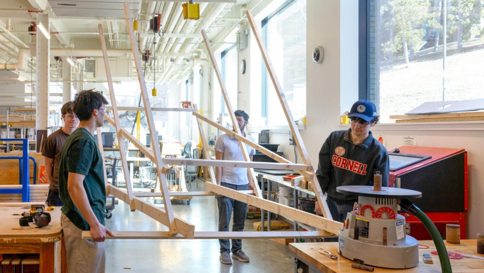 Four people hold a structure made from 2 by 4 lumber.