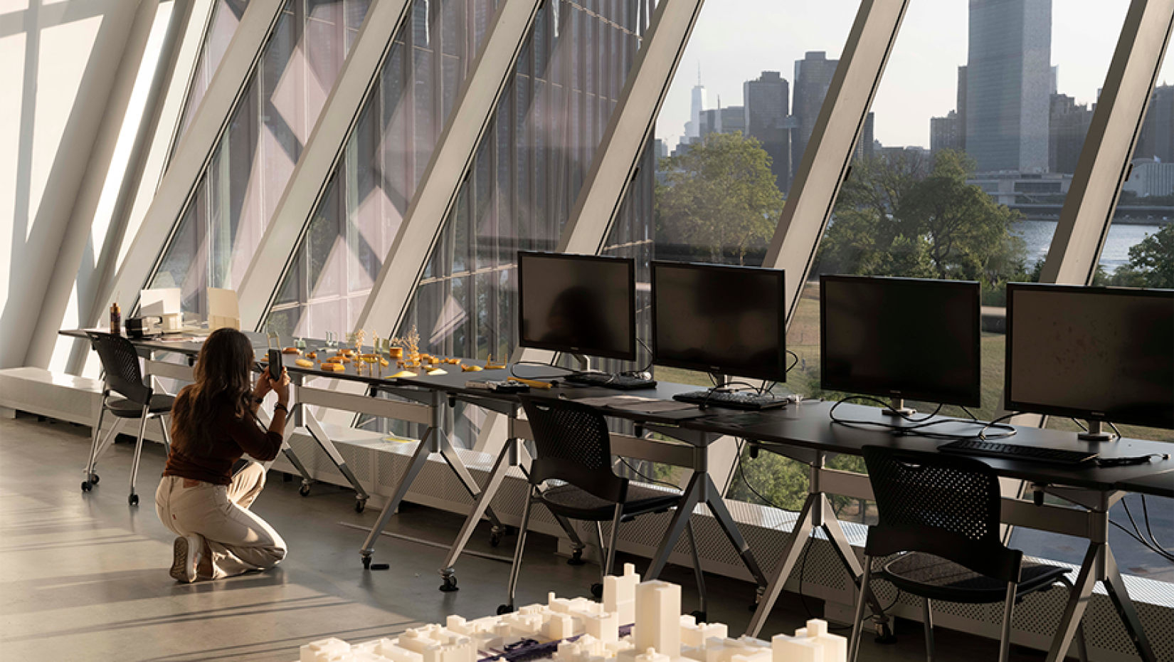 a person kneeling down taking a photo of an architectural city model on a table.