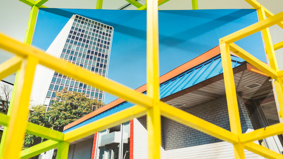 yellow metal grid over a photo of a tall white building against a blue sky