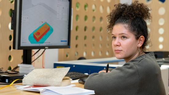 A person sitting a desk with books and a computer screen in front of them.