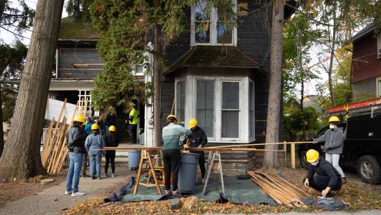People wearing yellow hardhats working on a construction project involving a home.