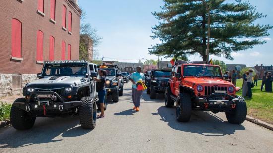 Jeep vehicles on a street with flags and people around them.