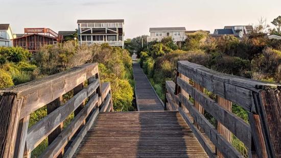 A wooden bridge leading to a row of houses surrounded by trees.