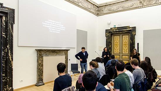 students seated in an ornate classroom with two lecturers in front