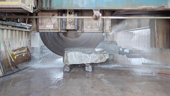 a large saw cutting a stone with water spewing from the cut area.