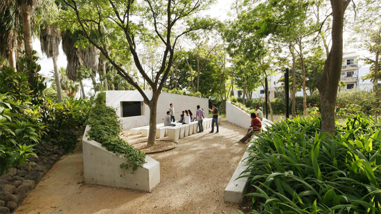 Area of white concrete seating tucked into a densely green area of a park