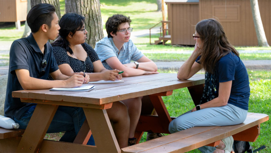 Four students seated at a wooden picnic table