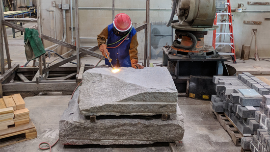 A person wearing a hardhat working with large stones and heavy machinery.