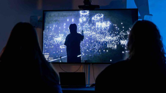 Two silhouettes of people sit in front of a television screen featuring visual works of art.