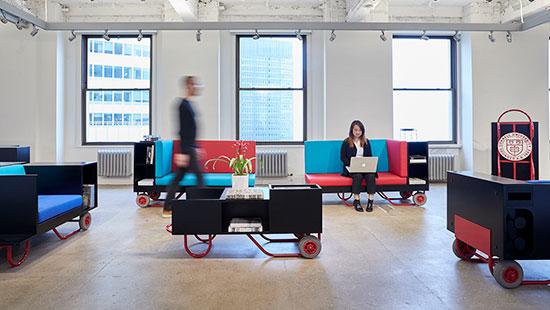 two students in the AAP NYC studio one sitting on colorful furniture, the other walking