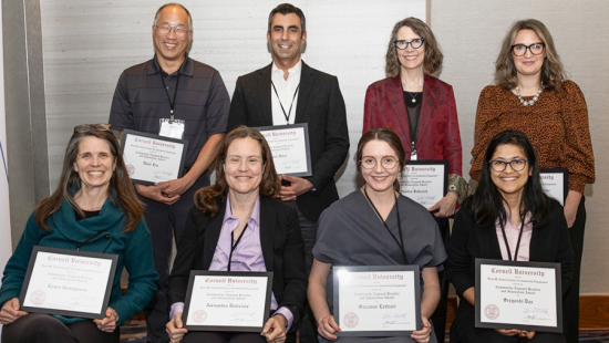 A group photo of the award recipients. Eight individuals in two rows of four, smiling.