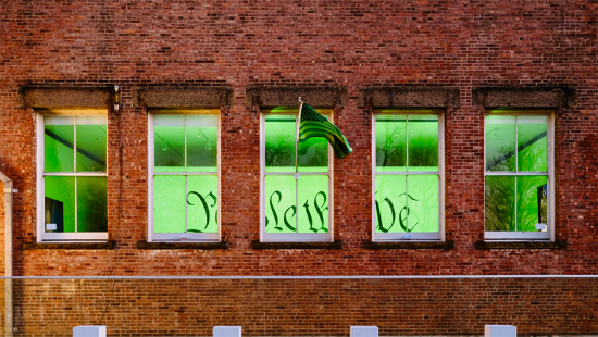 view through windows of a brick building of artwork lit by green light