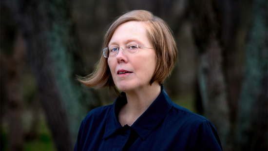 Woman with chin-length strawberry blonde hair wearing a blue jacket in a dark forest