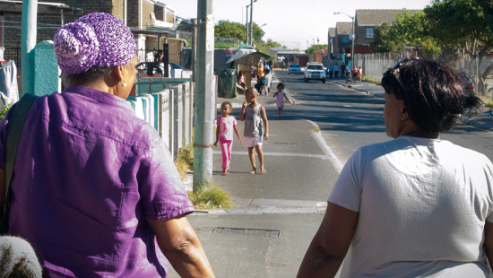 Women walking away from the camera along an urban street with children in the distance