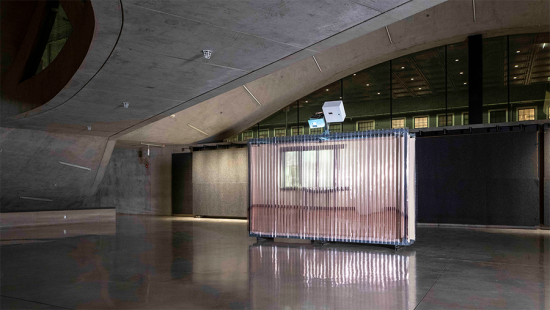 Large translucent textured wall in a large concrete space lit by projected light